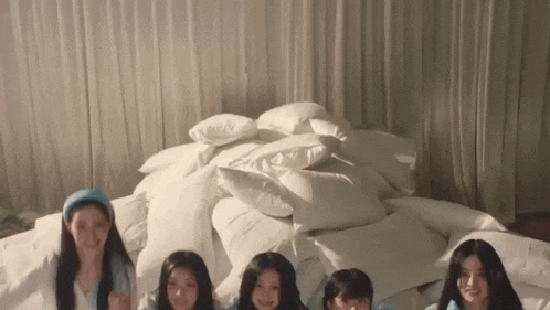 a group of young women are laying on a bed with a pile of pillows .