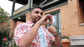 a man in a hawaiian shirt is sitting at a table eating a muffin .