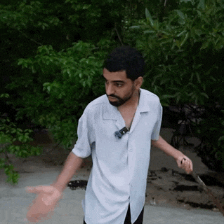 a man with a beard wearing a white shirt is standing on a beach with his arms outstretched