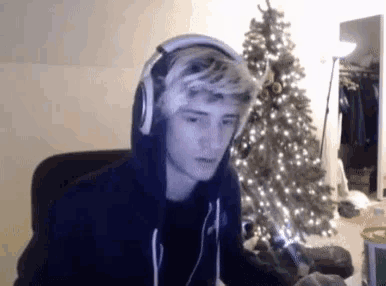 a young man wearing headphones is sitting in front of a christmas tree ..