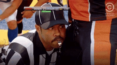 a referee with a whistle in his mouth watches a football game between the rhinos and cougars
