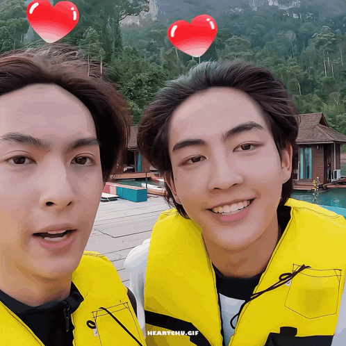 two young men wearing yellow life vests are posing for a picture with hearts above their heads and the words heartchu.gif below them