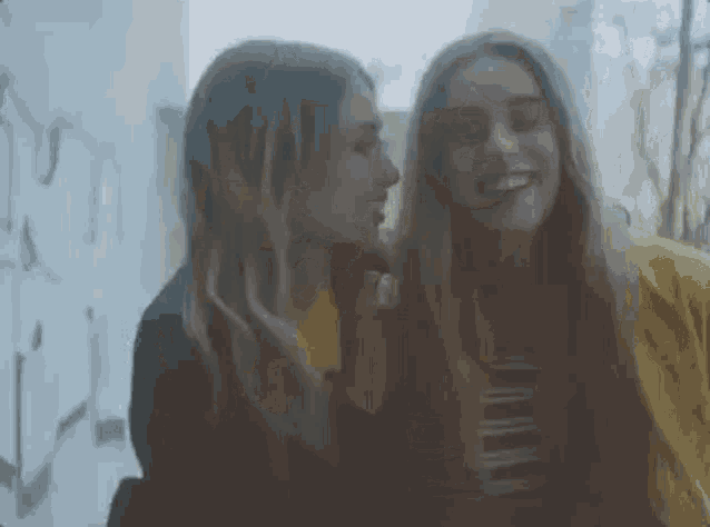 two young women are whispering into each other 's ears .