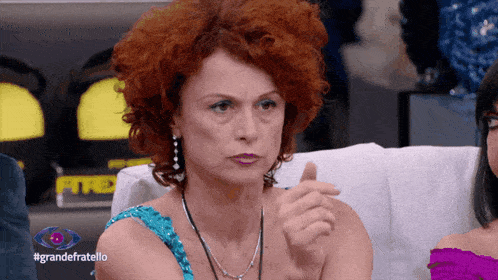 a woman with red hair is sitting on a couch with #grandefratello written on the bottom