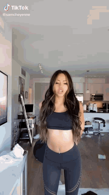 a woman in a crop top and leggings is standing in front of a mirror in a room .
