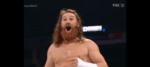 a shirtless wrestler with a beard and long hair is making a funny face .