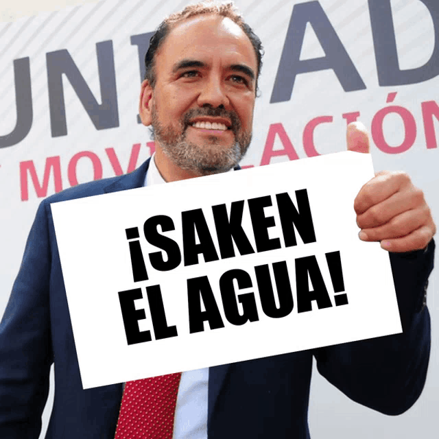 a man in a suit and tie holds up a sign that says isaken el agua