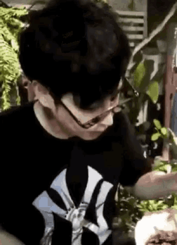 a man wearing glasses and a black shirt with a ny logo on it is holding a plant .