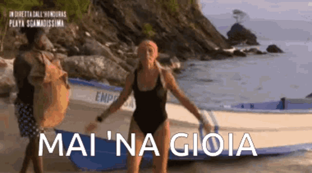 a woman in a swimsuit is standing on a beach next to a boat and says mai 'na gioia