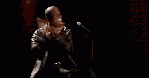 a man is sitting in front of a microphone in a dark room and making a funny face .