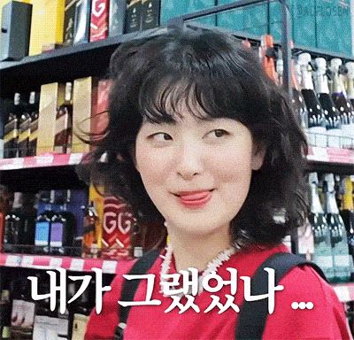 a woman in a red shirt is making a funny face in front of a shelf of alcohol