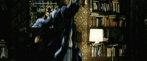 a man in a blue jacket is holding a gun in a room with a bookshelf .