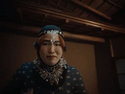 a woman wearing a head scarf and a hijab holds her hands together and looks at the camera