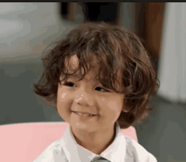 a young boy with curly hair and a white shirt and tie is smiling .