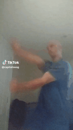 a man in a blue shirt is dancing in front of a wall with the words tiktok @capitalswag below him