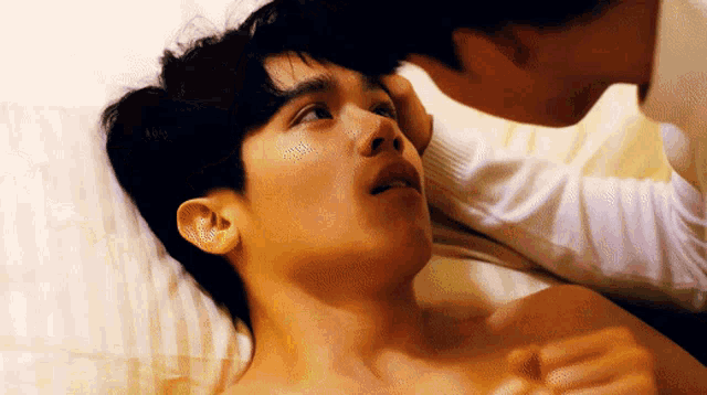 a man is touching another man 's forehead while laying on a bed
