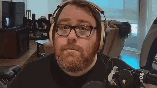a man with a beard and glasses is wearing headphones and looking at the camera .