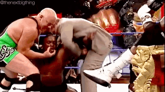 two men are wrestling in a wrestling ring while a man in a suit is kneeling down .