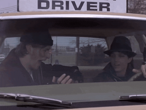 two men are sitting in a car with a sign that says driver