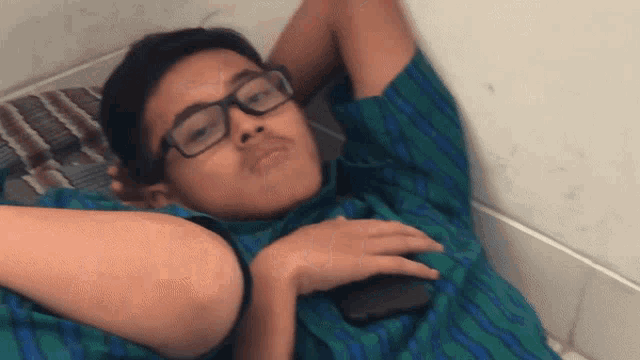 a young boy wearing glasses and a green shirt is laying down