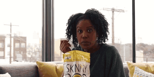 a woman sitting on a couch eating a bag of skinny doritos