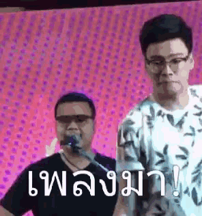 two men are standing next to each other in front of a microphone with a pink background .