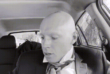 a bald man in a suit and tie is sitting in a car