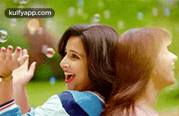 two women are playing with soap bubbles in a park and one of them is blowing soap bubbles .
