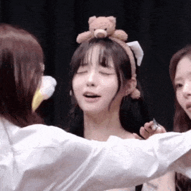 a girl with a teddy bear on her head is being hugged by another girl .