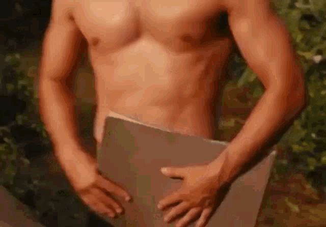 a shirtless man is holding a piece of cardboard in front of his stomach .