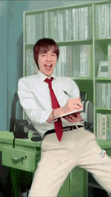 a man in a white shirt and red tie is holding a notebook
