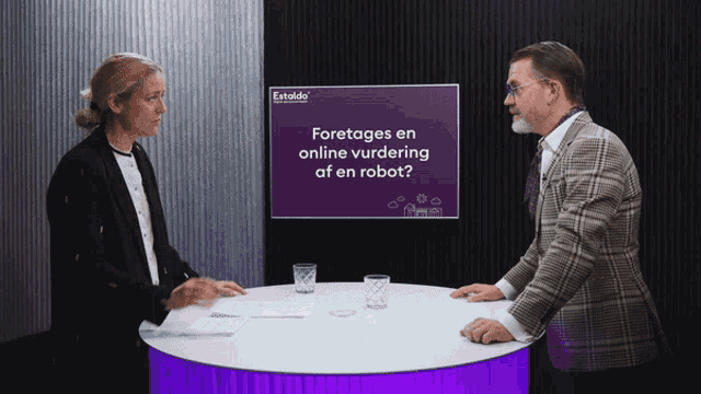 a man and a woman sit at a table in front of a screen that says " foretages en online vurdering af en robot " on it