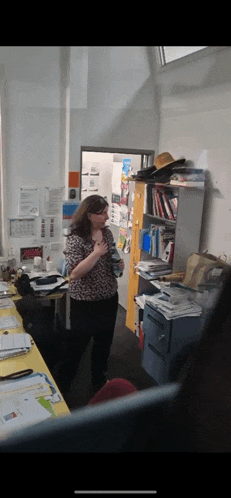 a woman in a leopard print shirt stands in a messy office
