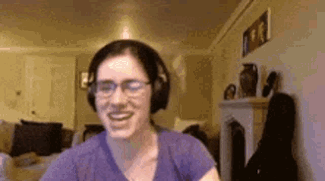 a woman wearing headphones and glasses is smiling while sitting in a living room .