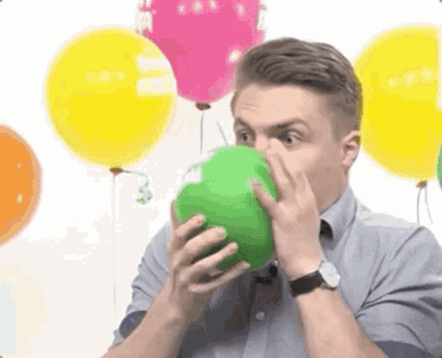 a man is blowing up a green balloon with his nose .