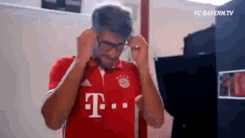 a man is wearing glasses and a red shirt with the letter t on it .