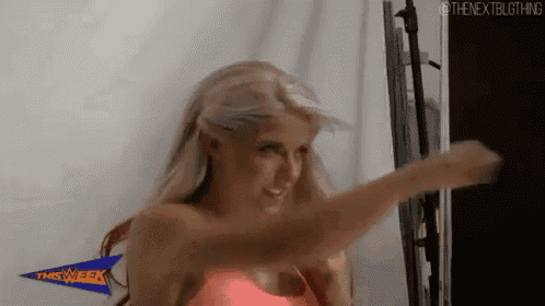 a woman in a pink tank top is standing in front of a wall and making a funny face .