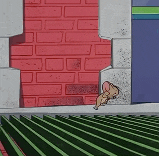 a cartoon mouse is standing in front of a brick wall and a green fence .