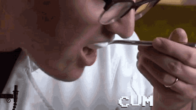 a person with glasses is eating something with a spoon and the word cum is visible in the background .