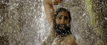 a man with a beard is taking a shower in a waterfall .