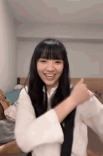 a young girl with long black hair and bangs is smiling and giving a thumbs up .