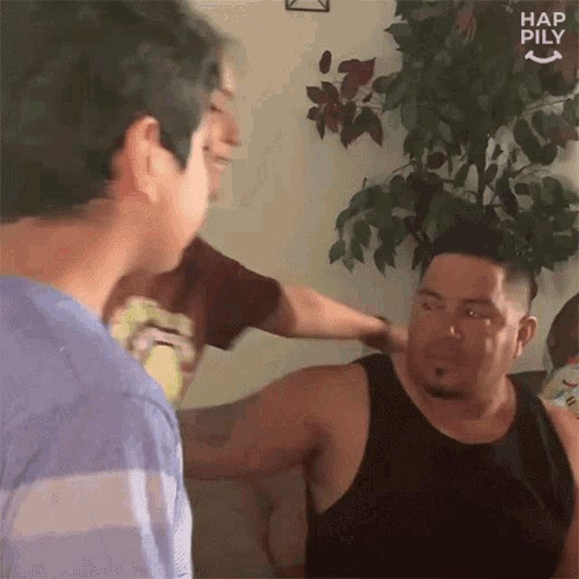 a man in a black tank top is standing next to another man in a living room .