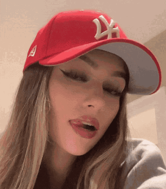a woman wearing a red ny hat is making a funny face .