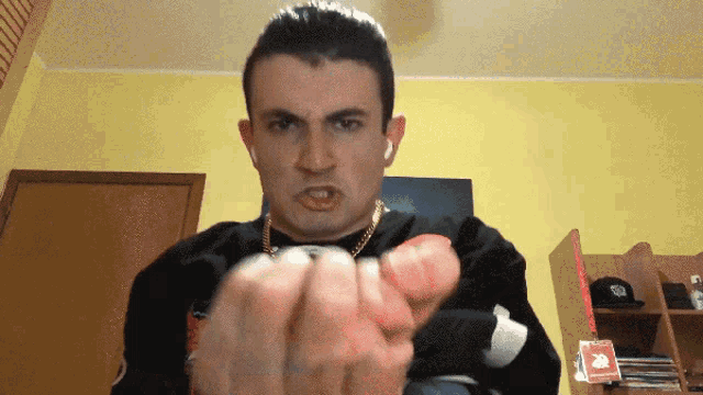 a man wearing a black sweater with a gold chain around his neck is making a face