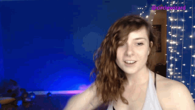 a woman in a grey tank top stands in front of a blue wall with the words @cirdewizard above her