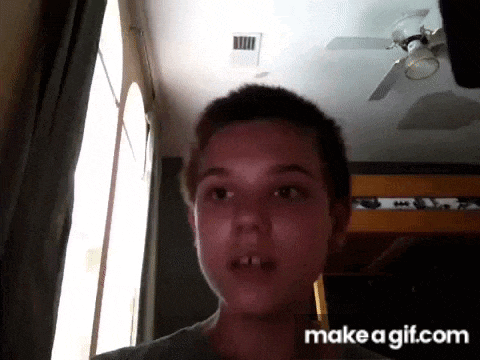 a young boy is standing in front of a window with a ceiling fan in the background .
