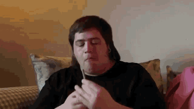 a man is sitting on a couch smoking a cigarette with a toothpick in his mouth .