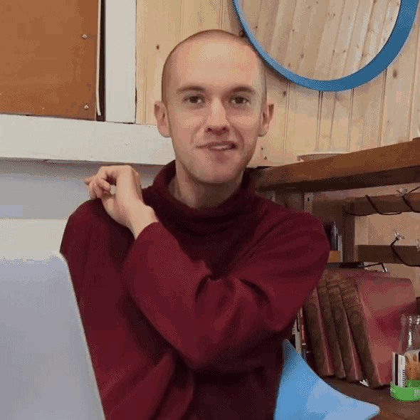 a bald man wearing a red sweater is sitting in front of a laptop