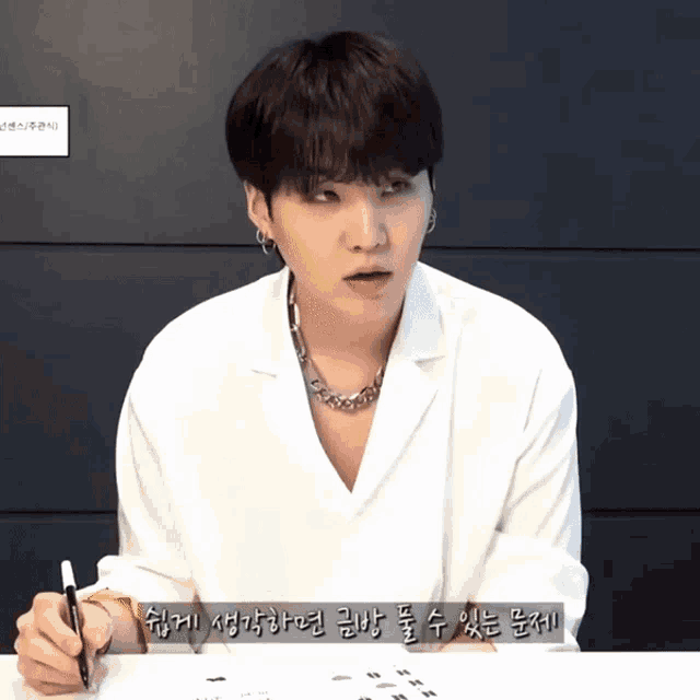a man in a white shirt is writing on a piece of paper with korean writing on it