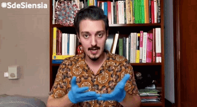 a man wearing blue gloves stands in front of a bookshelf with the hashtag #sdesiensia